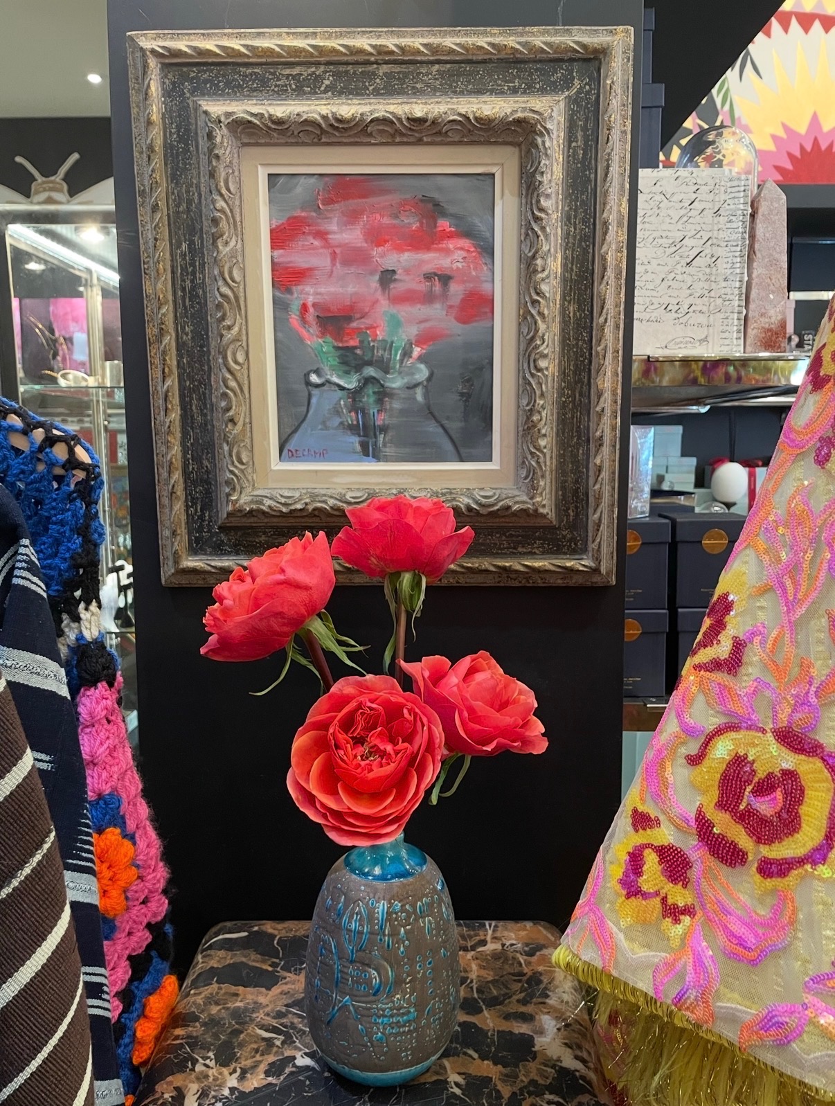 Annie Decamp red floral painting in an ornate frame above a vase of roses
