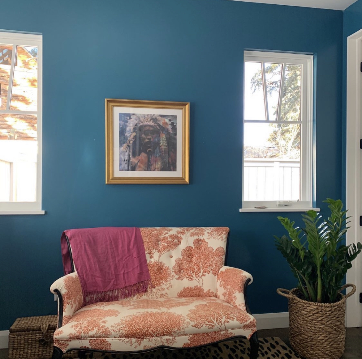Annie Decamp portrait painting hung on a deep blue wall above a settee