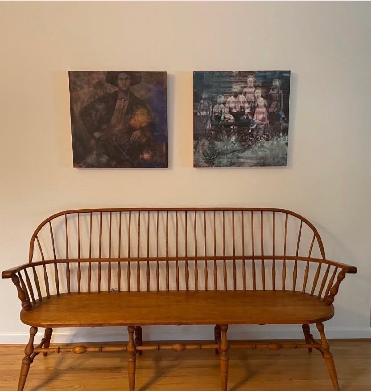 Two dark figurative Annie Decamp paintings on a white wall above a wooden bench