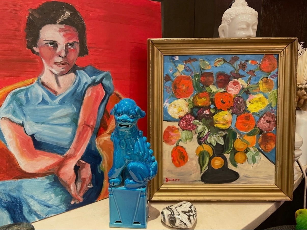 Annie Decamp portrait and floral still life paintings displayed with a blue foo dog