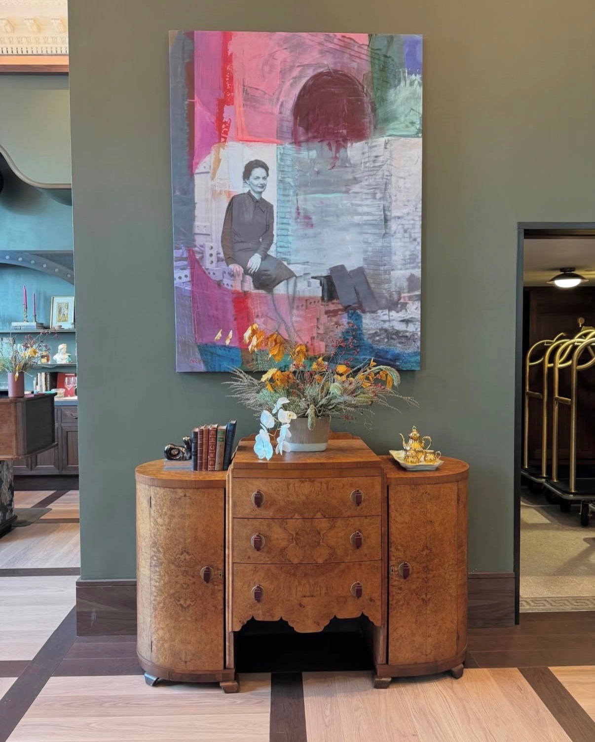 Annie Decamp mixed-media portrait displayed above a wooden cabinet in a hotel lobby